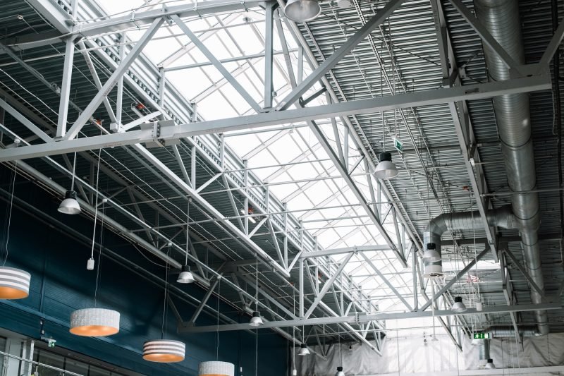 Metal roof structure of a large building, indoors. Built-in windows at the top for lighting